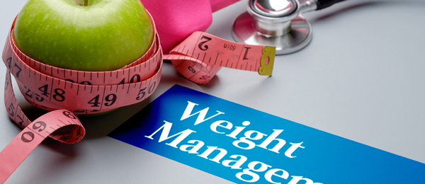 Green apple wrapped in a tape measure beside a stethoscope and a weight management sign